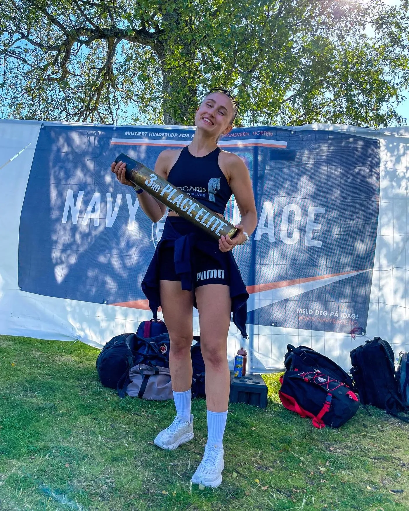 Midgard-løper smiler med pokalen for tredjeplass i eliteklassen foran NavyRace-banneret
